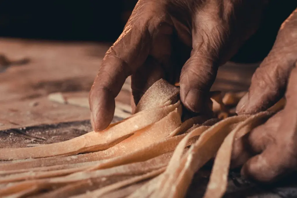 Hands shaping fresh pasta on a flour-dusted surface